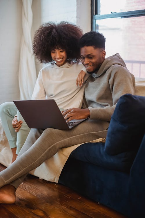 Cheerful black couple using laptop at home in daylight