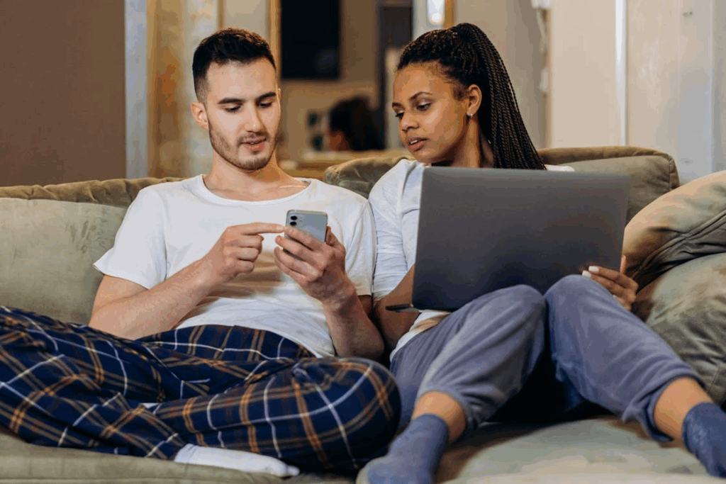 A Woman Holding a Laptop Beside a Man Holding a Cellphone