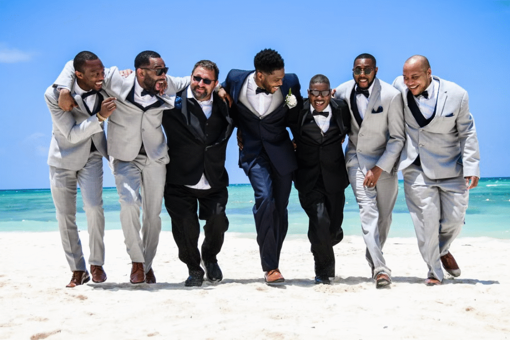 Group of smiling groomsmen enjoying a beach day together, dressed in formal attire.