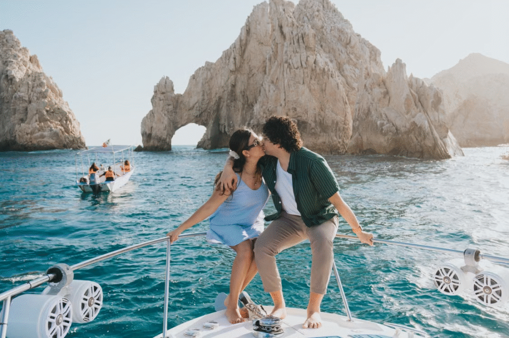 A couple shares a romantic kiss on a boat near the iconic Arch of Cabo San Lucas, Mexico.