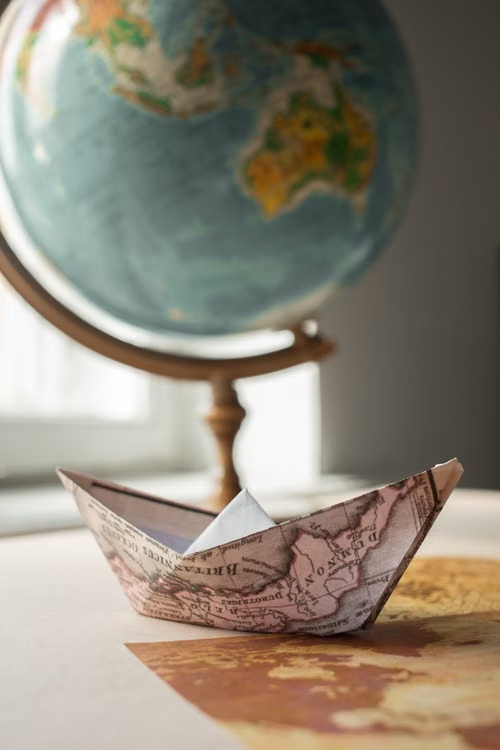 An origami boat made from a map rests near a globe, symbolizing global travel and exploration